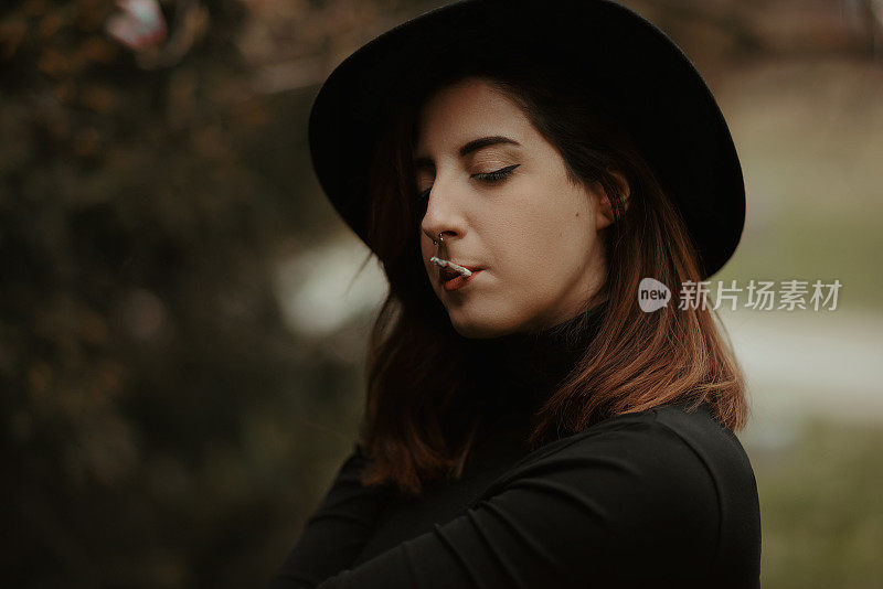 Young woman portrait wearing black hat and sweater and smoking cigarette with eyes closed